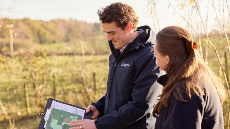 Two Environment Bank land managers at at Habitat Bank, looking over a clipboard with a map of the site, a man and a woman in their twenties