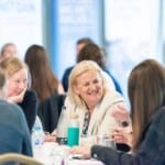 Two Environment Bank employees smiling together at a table at summer conference in 2023, both in their fifties with blonde hair
