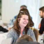 Environment Bank employee sat laughing at summer conference, a woman in her thirties with long, straight brown hair and glasses