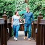 Two Environment Bank employees crossing a bridge together, one a man in his forties and the other a woman in her thirties, both wearing jeans and casual blue shirts