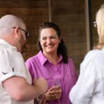 Three Environment Bank employees dressed casually and chatting together with glasses of champagne at summer party in 2024, aged between thirty and sixty