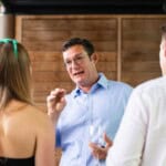 Environment Bank employee in his fifties wearing a smart blue button-up shirt, mid-conversation at summer party in 2024