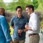 Three Environment Bank employees chatting together with drinks at summer party, all men in their thirties