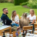 Four Environment Bank employees in their twenties and thirties dressed casually and sat chatting together at summer party drinks reception