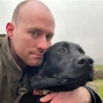 Wally, a black Labrador, being cuddled by Henry, Environment Bank's Chief Revenue Officer