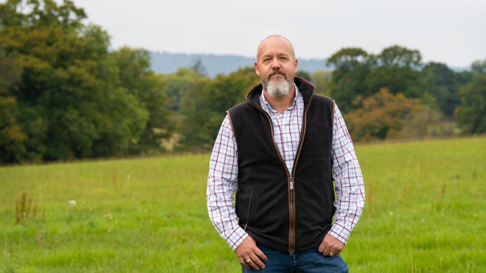 Environment Bank's landowner partner, Jon, at Chiddingfold Habitat Bank wearing a check shirt and body warmer